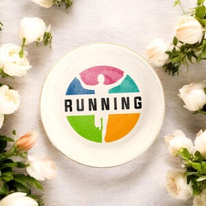 May include: White ceramic dish with a gold rim. The dish features a colorful graphic of a running person with the word "RUNNING" in black text.