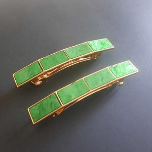 May include: Two gold-tone metal hair barrettes featuring a curved rectangular shape. Each barrette is inlaid with three distinct segments of bright green marbled acrylic material, creating a smooth, polished surface with a metallic border.