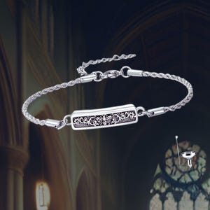 May include: A silver bracelet with a delicate chain and a rectangular charm featuring an intricate floral design with a bee in the center.