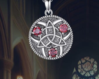 Può includere: Collana con ciondolo in argento con un designo a nodo celtico e tre pietre preziose rosse. Il ciondolo è rotondo e ha una superficie dettagliata e testurizzata.