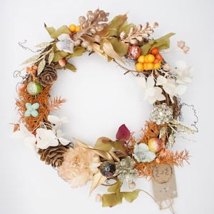 May include: A fall-themed wreath with a variety of dried flowers, berries, and pine cones. The wreath is decorated with gold glitter and has a brown paper tag with the text "Made with Love".