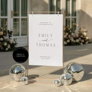 May include: A wedding welcome sign with a copper frame displays the names "Emily and Thomas" and event details. The sign is accompanied by disco balls of varying sizes. The text reads "Welcome to the wedding of" and "Weston Hall 20.12.2023".