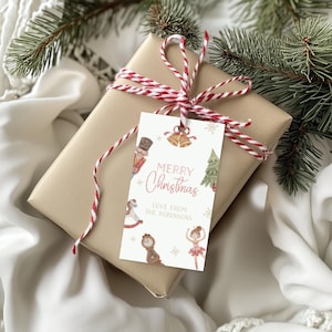 以下が含まれることがあります： 茶色の紙で包まれ、赤と白の紐で結ばれたクリスマスプレゼント。タグには「Merry Christmas」と書かれており、くるみ割り人形、ベル、クリスマスツリー、バレリーナなどのお祝いのイラストが描かれています。