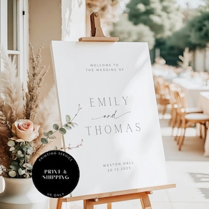May include: A white wedding welcome sign on a wooden easel. The sign reads "Welcome to the Wedding of Emily and Thomas" with the date 20.12.2023 and location Weston Hall. A black circle with text "PRINT & SHIPPING UK ONLY" is in the lower left.