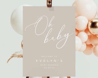 Op de afbeelding: Een beige welkomstbord met witte kalligrafie die "Oh baby" en de tekst "Welkom op Evelyns babyshower 09.04.24" zegt.