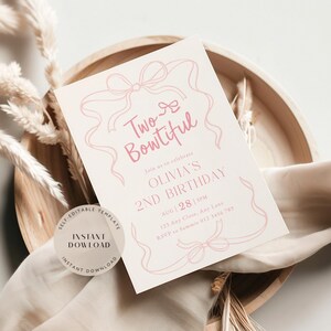 May include: A light pink and cream-coloured invitation for a second birthday party. The invitation features the text "Two-Bowtiful" and details for Olivia's 2nd birthday, including the date, time, and RSVP information. The invitation is on a wooden tray with decorative elements.
