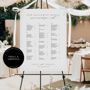 May include: A white wedding seating plan on a black easel, with the text "OUR FAVOURITE PEOPLE we've saved you a seat." Names are listed alphabetically. The bottom reads "Emily and Thomas 15th August 2023."