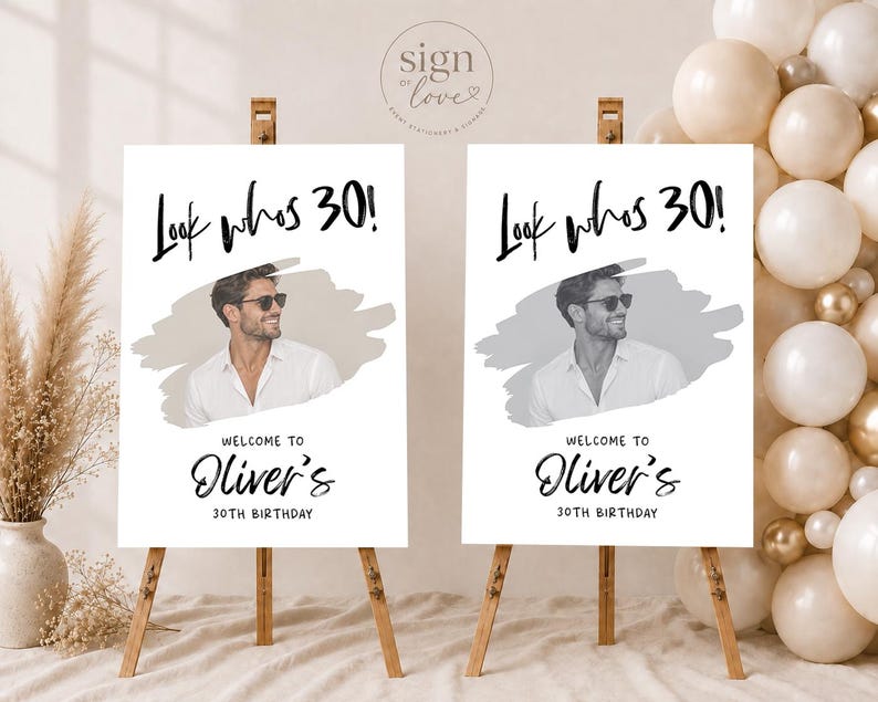 May include: Two white rectangular birthday signs on wooden easels. Each sign features the black text "Look whos 30!", a central photo of a person in a white shirt and sunglasses, and the text "WELCOME TO Oliver's 30TH BIRTHDAY" in black lettering.