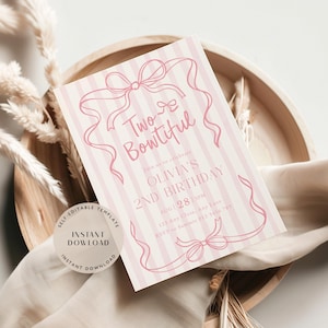 May include: A pink and white striped invitation card with the text "Two Bowtiful" and "Olivia's 2nd Birthday". The card features bow and ribbon illustrations. The card is on a wooden tray with decorative elements.