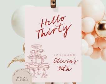 May include: A pink sign with the words "Hello Thirty" in red script. Below, it reads "Let's Celebrate Olivia's 30th." A drawing of champagne glasses is on the bottom left. The sign is propped up on a wooden easel, with balloons in the background.