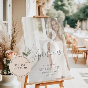 Op de afbeelding: Een bord voor een 18e verjaardag met een foto van een jonge vrouw en de tekst "Amelia is". Het bevat ook "Welkom op Amelia's 18e verjaardagsfeest 16.03.2025". Het bord staat op een houten ezel.
