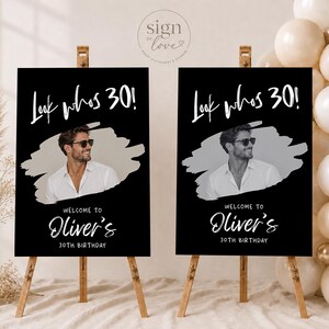 May include: Two identical black rectangular birthday signs on wooden easels. Each sign features the white text Look whos 30!, a central grayscale photo of a person wearing sunglasses and a white shirt, and the text Welcome to Oliver's 30th Birthday.