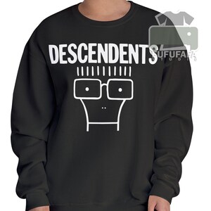 Może przedstawiać: Czarna bluza z napisem "DESCENDENTS" w białych literach nad białą twarzą z kreskówki w okularach. Projekt to prosta, odważna grafika.