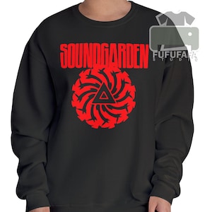 May include: Black sweatshirt with the red text "SOUNDGARDEN" above a red circular design with a triangle in the center. The design is a stylized graphic. The sweatshirt is a crew neck style.