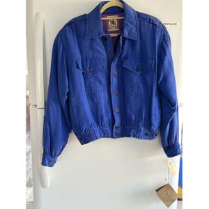 Peut inclure: Une veste bleu vif dotée d'un col classique, de manches longues avec poignets boutonnés et d'une fermeture à boutons sur le devant. Le vêtement comprend deux poches poitrine à rabat boutonné, des épaulettes et une doublure intérieure violette.
