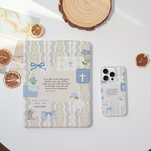 May include: A patterned journal and phone case set. The journal and phone case feature a light blue and beige floral design with a cross and the text "It is the Lord who goes before you, he will be with you..."