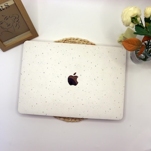 Op de afbeelding: Witte laptop met een gespikkeld ontwerp en een Apple-logo op de deksel. De laptop staat op een geweven mat.