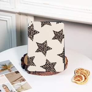 May include: A cream tablet case with a pattern of leopard print stars. The case is displayed on a wooden base, with dried lemon slices in the background. The case is designed to protect a tablet.