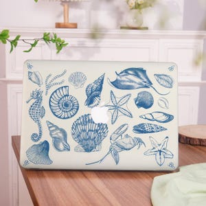 May include: A white laptop with a blue and white seashell design. The design features a variety of seashells, starfish, a crab, a stingray, and a seahorse.