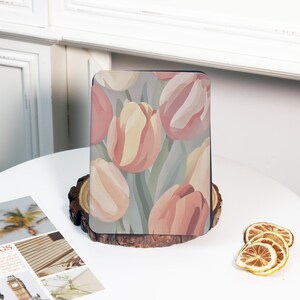 May include: A rectangular case featuring a floral design of pink, peach, and yellow tulips on a light blue background. The case is displayed on a wooden slice, with dried lemon slices and a magazine visible.