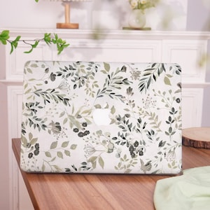 May include: A white laptop case with a green and gray floral pattern. The case has a cut-out for the Apple logo.