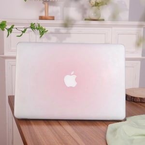 Puede incluir: Un ordenador portátil blanco con un degradado rosa en la tapa. El logotipo de Apple es visible en la tapa.