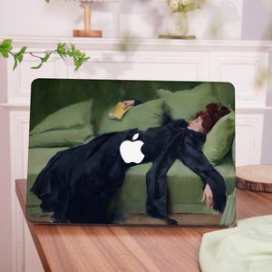 May include: Laptop case featuring a painting of a woman in a black dress reclining on a green sofa, holding a book. The Apple logo is prominently displayed. The artwork has a classic, vintage aesthetic.
