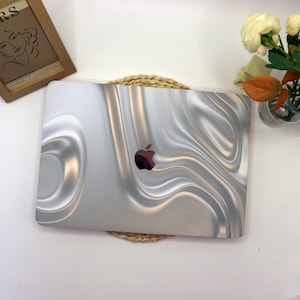 May include: A silver laptop with a white and gold swirl design. The laptop has an Apple logo on the lid.
