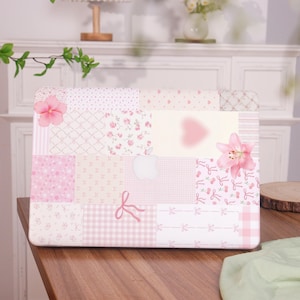 May include: A pink and white patchwork laptop case with various patterns including flowers, hearts, and bows. The case features a light pink Apple logo and is adorned with pink flowers. The design is feminine and decorative.