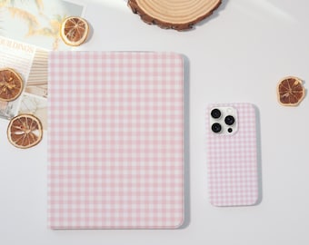 Può includere: Una custodia per tablet e una custodia per telefono con motivo a quadretti rosa e bianco. Le custodie sono su una superficie bianca con fette d'arancia essiccate e un sottobicchiere di legno. La custodia del tablet è rettangolare.