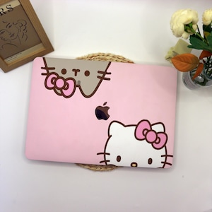 May include: Pink laptop case with a Hello Kitty and a Pusheen cat design. The case has a white Apple logo.