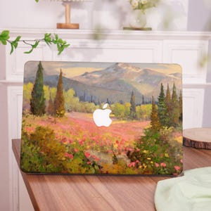 May include: A laptop skin with a painted landscape scene. The image features a field of flowers in the foreground, with trees and mountains in the background. The sky is a soft blue with clouds. The laptop skin is designed to fit a standard laptop.