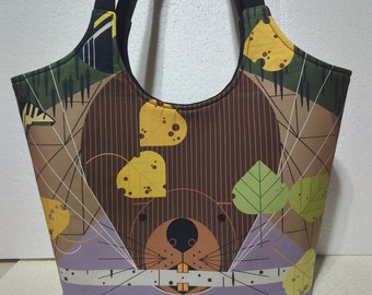 May include: A tote bag featuring a beaver design. The bag has a brown and purple base with a beaver face, yellow cheese, and green leaves. The handles are black, and the bag has a structured shape.