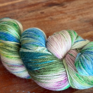 May include: A close-up of a skein of colorful yarn. The yarn is a blend of blues, greens, pinks, and yellows. The yarn is tightly wound and has a soft, textured appearance. The yarn is likely used for knitting or crocheting.