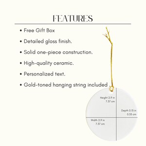 May include: A white ceramic ornament with a gold-toned hanging string. The round ornament has a height and width of 7.37 cm and a depth of 0.33 cm. The image includes text that reads "FEATURES" and lists features such as "Free Gift Box" and "Personalized text."
