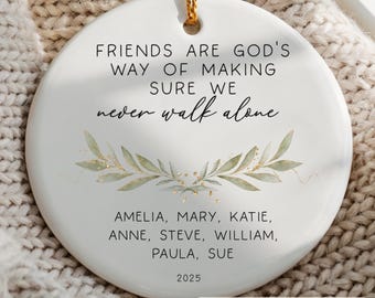 May include: A white ceramic ornament with gold string for hanging. The ornament features the text "FRIENDS ARE GOD'S WAY OF MAKING SURE WE never walk alone." Below the text are the names AMELIA, MARY, KATIE, ANNE, STEVE, WILLIAM, PAULA, SUE, and the year 2025.