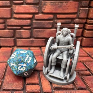 May include: A gray miniature figure of a person in a wheelchair, holding a bar, next to a blue and green speckled twenty-sided die. The background is a brick wall and a brick-patterned surface.