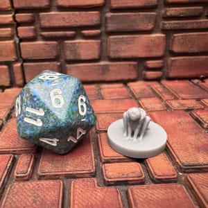 May include: A blue and green marbled D20 die with white numbering next to a grey miniature figure on a circular base. The die shows the number 6. The background is a brick-like pattern.