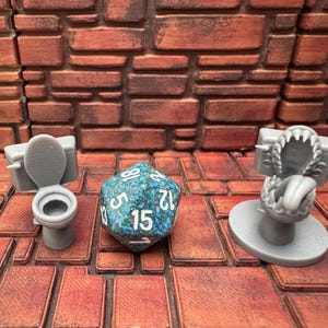 May include: A gray miniature toilet and a monster toilet with a large blue and green d20 die. The die has white numbers. The background is a brick wall and brick floor.