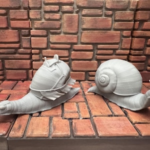 May include: Two gray snail figurines, one with a helmet and armor, the other with a simple shell. The snails are on a brick-like surface with a brick wall background. The figurines are detailed.