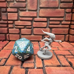 Puede incluir: Una figura en miniatura gris de un personaje corriendo con el pelo suelto, junto a un dado grande de múltiples caras con patrones azules y verdes y números blancos. El fondo es una pared de ladrillos.