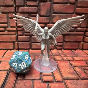May include: A gray figurine of a winged figure holding a staff, standing on a clear base. A multi-sided blue and green die with white numbers is in the foreground. The background is a brick wall.