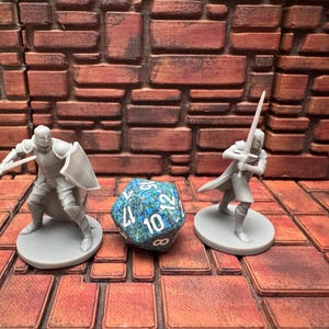 May include: A tabletop role-playing game set featuring two miniature knight figurines with swords and shields, and a multi-sided die. The die is blue and green with white numbers. The miniatures are grey.