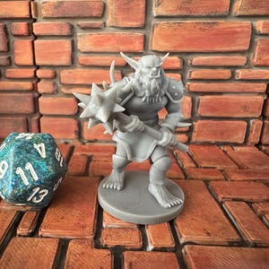 Op de afbeelding: Een grijs plastic miniatuurfiguur van een fantasiewezen met een geknotte knots. Het wezen heeft een baard en hoorns. De miniatuur staat op een grijze basis.