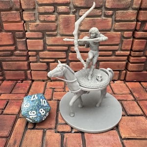 Könnte beinhalten: Graue Miniaturfigur eines Bogenschützen, der auf einem pferdeähnlichen Wesen mit einer runden Plattform steht. Der Bogenschütze zielt mit Pfeil und Bogen. Ein blau-grüner 20-seitiger Würfel befindet sich im Vordergrund. Der Hintergrund ist eine Backsteinmauer.