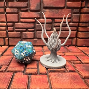 May include: A light gray, 3D-printed fantasy miniature of a tree-like creature with four upward-curving tendrils. Next to it is a multi-colored, 20-sided die with white numbers. The objects are on a brick-patterned surface.