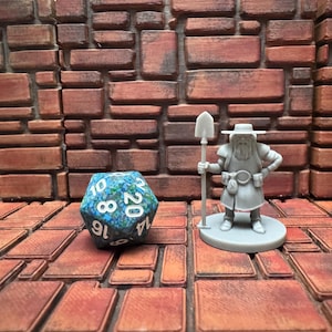 May include: A tabletop scene featuring a blue and white twenty-sided die and a miniature figurine of a bearded man holding a shovel. The background is a brick wall and floor, creating a fantasy game setting.