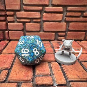 May include: A blue and green speckled twenty-sided die with white numbers sits next to a miniature gray rat figurine holding a scythe. The items are on a brick-patterned surface.