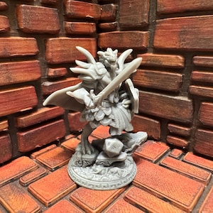 Op de afbeelding: Een grijs, gedetailleerd miniatuurbeeldje van een draakachtig wezen dat een harnas draagt en een zwaard vasthoudt. Het beeldje staat op een voetstuk met een dobbelsteen.