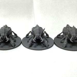May include: Five dark grey miniature insectoid figures with spiky carapaces, multiple legs, and prominent mandibles. Each creature is mounted on a circular base, displaying a textured, armoured exoskeleton design with sharp, pointed details.